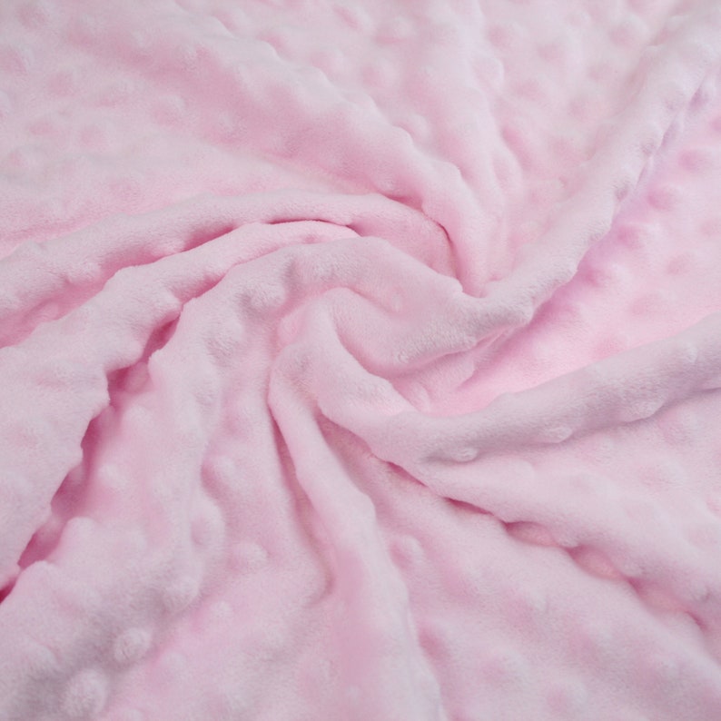 May include: A soft, pink fabric with a textured, dotted pattern. The fabric is folded and draped, showing its texture and colour.
