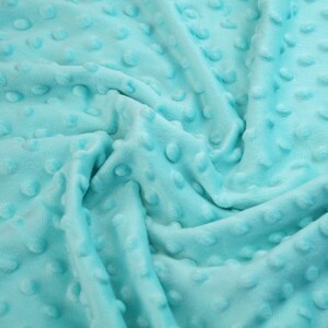 May include: A close-up of a soft, turquoise blue fabric with a textured, dotted pattern. The fabric is wrinkled and folded, showing the texture of the material.