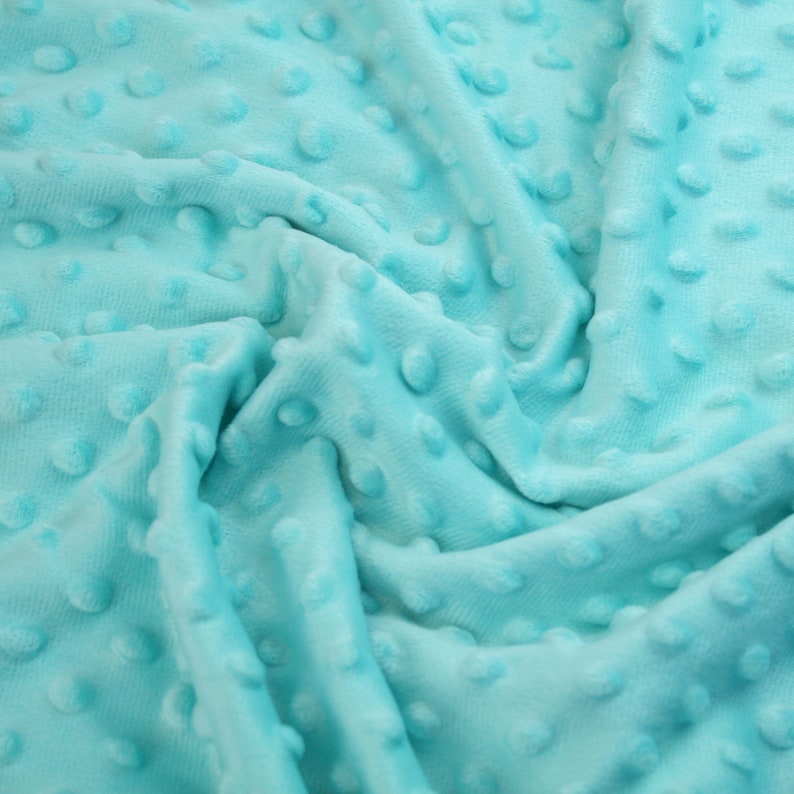 May include: A close-up of a soft, turquoise blue fabric with a textured, dotted pattern. The fabric is wrinkled and folded, showing the texture of the material.