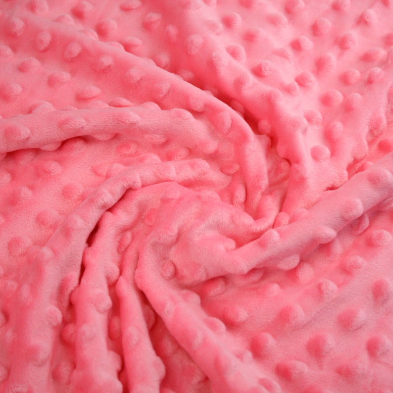 May include: Pink textured fabric with a soft, fuzzy surface. The fabric has a raised dot pattern.