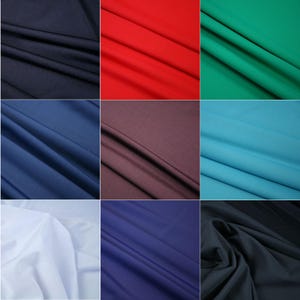 Op de afbeelding: Een verzameling stofstalen in verschillende kleuren, waaronder marineblauw, rood, groen, bruin, lichtblauw, wit, donkerblauw en zwart. De stofstalen zijn gerangschikt in een rasterpatroon.