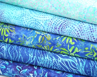 May include: A stack of five blue and green batik fabric squares with different patterns. The top fabric is light blue with a white and light blue pattern. The second fabric is a darker blue with a white and blue pattern. The third fabric is a dark blue with a green and blue pattern. The fourth fabric is a dark blue with a white and blue pattern. The bottom fabric is a dark blue with a purple and blue pattern.