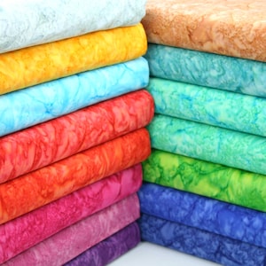 Op de afbeelding: Een stapel kleurrijke vierkante stoffen met een marmerpatroon. De stof is in tinten blauw, groen, geel, oranje, rood, roze en paars.