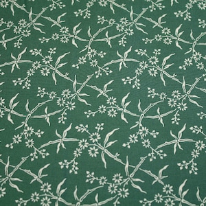 Könnte beinhalten: Ein grüner Stoff mit einem weißen Blumenmuster. Das Muster zeigt kleine Blumen und Blätter, die in einem sich wiederholenden Design angeordnet sind.