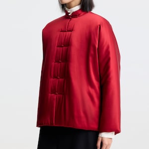 May include: A red satin jacket with a mandarin collar and a button closure. The jacket has a quilted design and is lined with a white fabric.