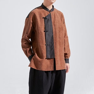 Può includere: Una camicia marrone a maniche lunghe con dettagli neri. La camicia presenta un colletto alla coreana, finiture nere sulle spalle, polsini e un pannello centrale con tre bottoni neri. Abbinata a pantaloni neri, crea un completo elegante.