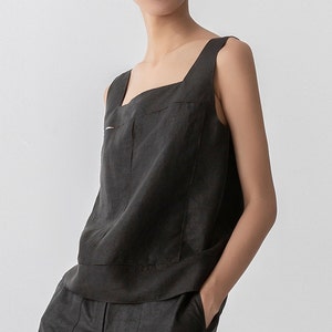 May include: A sleeveless, dark gray linen top with a square neckline and a straight hem. The top has a small pocket on the front.