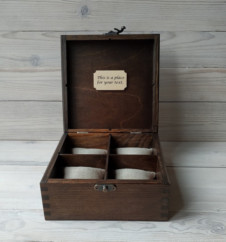 May include: A dark brown wooden box with a hinged lid and a small metal latch. The box has six compartments lined with beige fabric. The lid has a small wooden plaque with the text "This is a place for your text."
