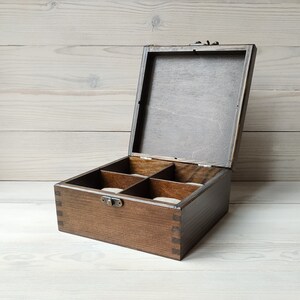 May include: A dark brown wooden box with a hinged lid and a brass latch. The box has five compartments lined with a light brown fabric.