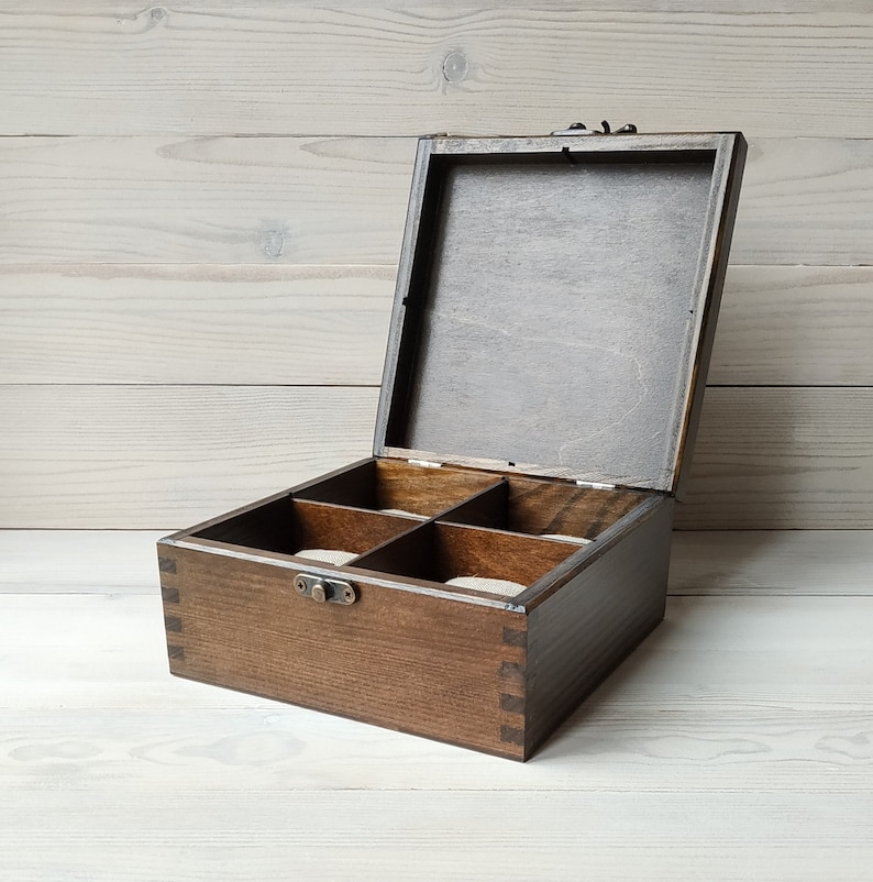 May include: A dark brown wooden box with a hinged lid and a brass latch. The box has five compartments lined with a light brown fabric.