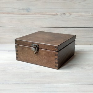 May include: A dark brown wooden box with a hinged lid and a metal latch. The box is made of solid wood and has a natural wood grain finish.