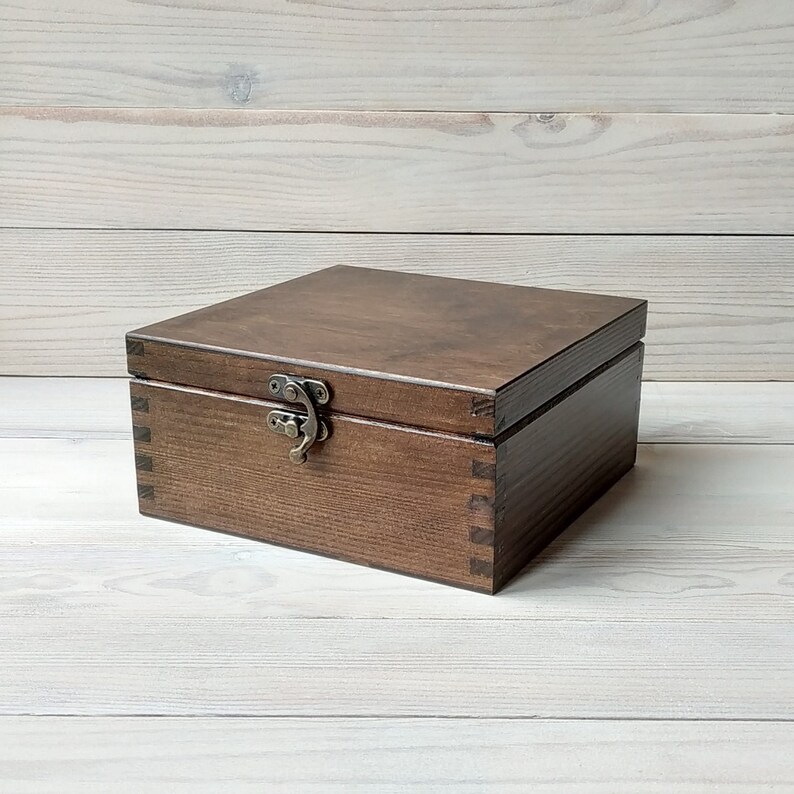May include: A dark brown wooden box with a hinged lid and a metal latch. The box is made of solid wood and has a natural wood grain finish.