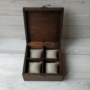 May include: A dark brown wooden box with a hinged lid and a metal latch. The box has four compartments lined with beige fabric.