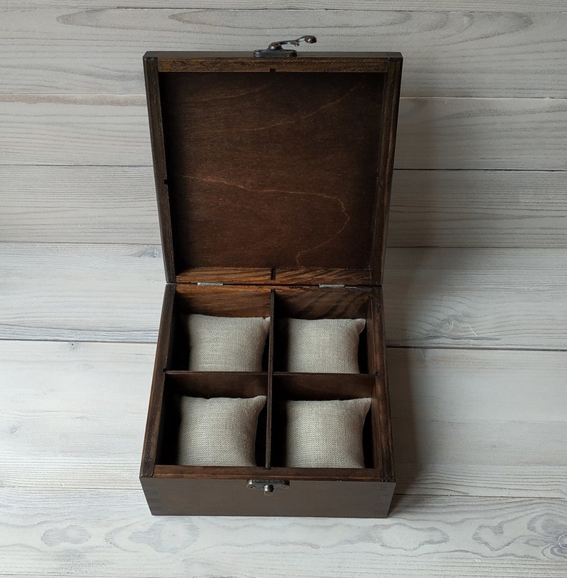 May include: A dark brown wooden box with a hinged lid and a metal latch. The box has four compartments lined with beige fabric.