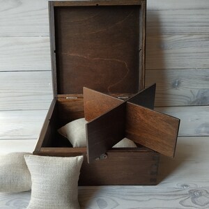 May include: A wooden box with a hinged lid and a divider inside. The box is open and there are three beige fabric cushions inside.