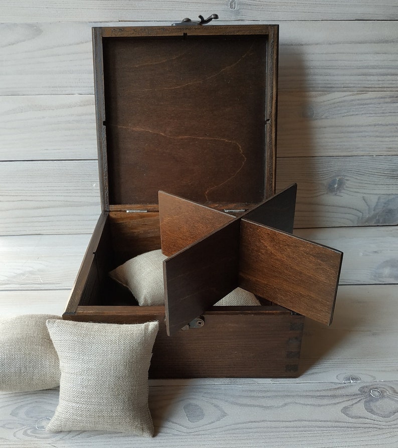 May include: A wooden box with a hinged lid and a divider inside. The box is open and there are three beige fabric cushions inside.