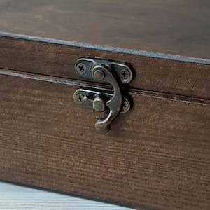 May include: A dark brown wooden box with a brass latch. The box has a wood grain pattern and is closed.
