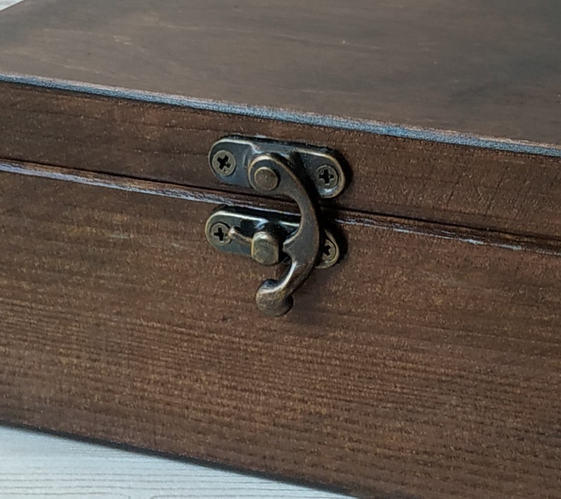 May include: A dark brown wooden box with a brass latch. The box has a wood grain pattern and is closed.