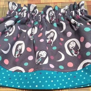 May include: A gathered skirt featuring a dark gray fabric with a repeating pattern of a female character with long dark hair, white crescent moons, and multicolored polka dots, finished with a teal hem band decorated with small white polka dots.