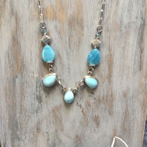May include: A silver chain necklace with blue gemstone beads. The necklace features a teardrop-shaped pendant with a silver setting.