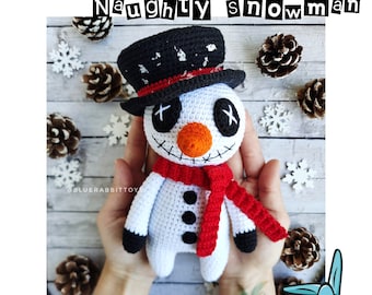 May include: A crocheted snowman amigurumi toy with a black top hat, red scarf, and black eyes. The snowman has a stitched mouth and a stitched X on each eye. The snowman is held in a person's hands against a woodgrain background.