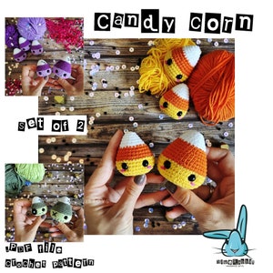 May include: A set of two crocheted candy corn amigurumi toys. The toys are orange, yellow, and white with black eyes and a smiling mouth. The toys are sitting on a wooden surface with colorful sequins.