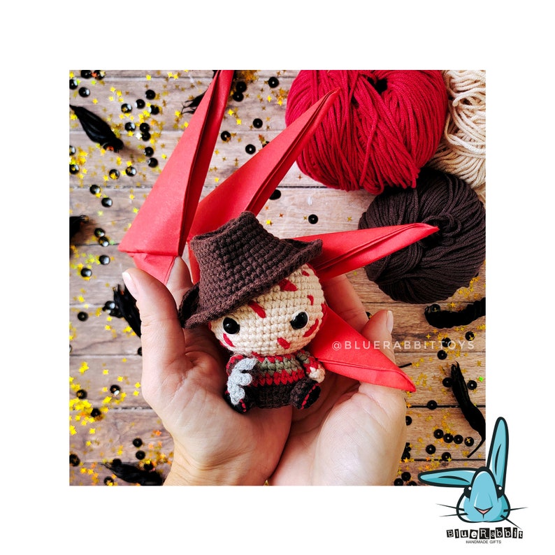 Peut inclure: Un jouet en crochet amigurumi de Freddy Krueger du film A Nightmare on Elm Street. Le jouet porte un chapeau brun et une chemise &agrave; rayures rouges et blanches. Le jouet est tenu dans les mains d'une personne.
