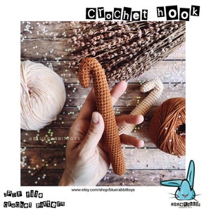 Può includere: Un uncinetto all'uncinetto marrone su uno sfondo di legno. L'uncinetto è tenuto in una mano. C'è un gomitolo di lana sullo sfondo.