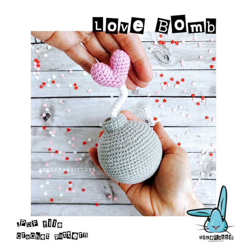 Puede incluir: Un juguete de bomba de ganchillo gris de forma esf&eacute;rica con una mecha blanca rematada por un coraz&oacute;n rosa. El texto "LOVE BOMB" aparece en la parte superior y "PDF file crochet pattern" abajo a la izquierda. Confeti rojo y blanco rodea el objeto.