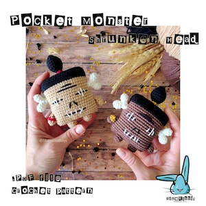 May include: Two crochet "Pocket Monster Shrunken Head" figures. One is tan with black accents, the other is brown with black accents. Both have white bone-like appendages and stitched facial features. The text "Pocket Monster Shrunken Head" is at the top.