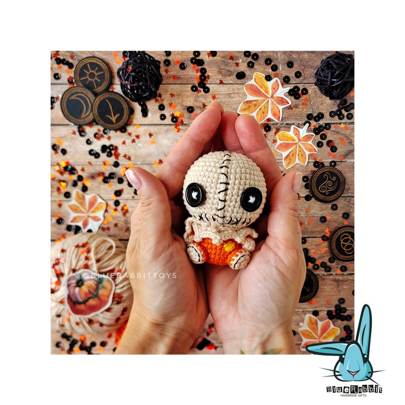 May include: A crocheted amigurumi doll with a stitched face, black button eyes, and a stitched mouth. The doll is wearing a brown and orange crocheted outfit. The doll is being held in a person's hands.