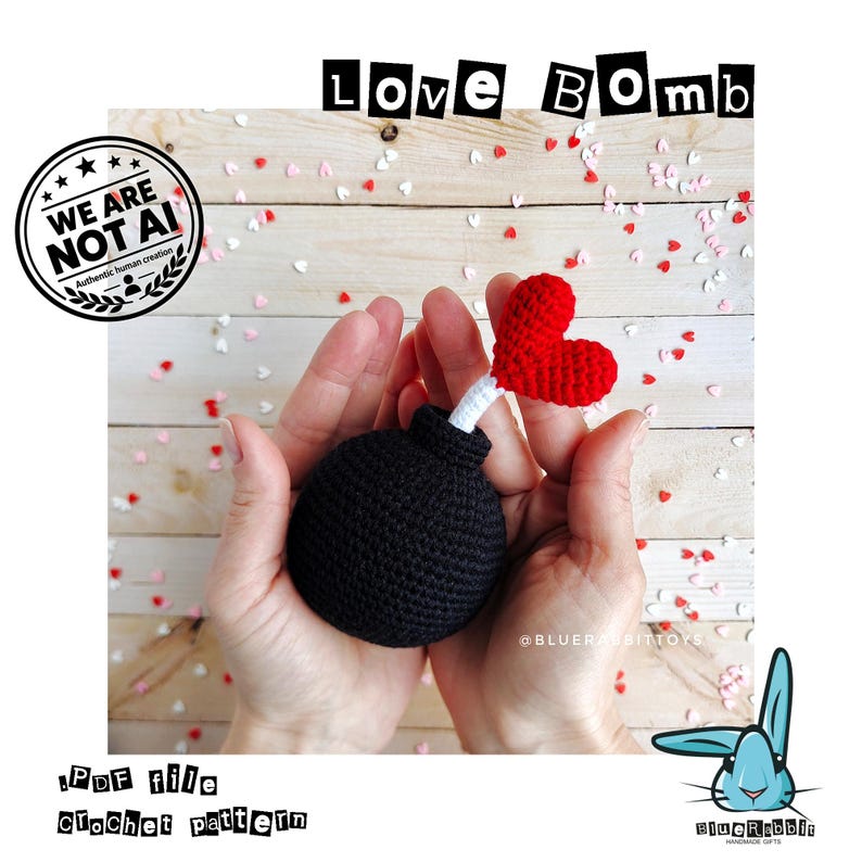 Puede incluir: Una esfera negra de ganchillo con forma de bomba, una mecha blanca y un coraz&oacute;n rojo de ganchillo en el extremo. El texto LOVE BOMB aparece arriba y el texto .PDF file crochet pattern abajo, con un sello de WE ARE NOT AI.