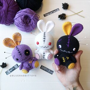 May include: Three crocheted bunny pincushions with stitched-on eyes and mouths. The bunnies are purple, white, and black with yellow ears. The pincushions are decorated with safety pins and have a stitched-on heart on their chests. The text "LOVE THIS" and "100% fun" are visible in the image. The text "THE DETAILS" is also visible in the image.