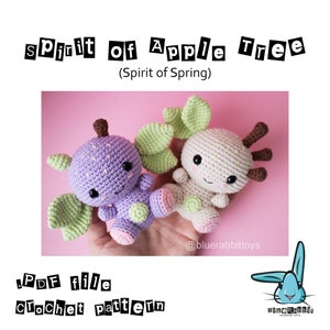 May include: Two crocheted amigurumi toys, one purple and one white, with green leaves and brown antlers. The purple toy is shaped like an apple and the white toy is shaped like a deer. The toys are on a pink background. The text "Spirit of Apple Tree (Spirit of Spring)" is at the top of the image. The text "PDF file Crochet pattern" is at the bottom of the image. The text "@bluerabbittoys" is in the lower right corner of the image.