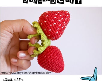 Puede incluir: Patrón de crochet para una fresa roja y verde. El patrón está disponible como archivo PDF. La imagen muestra una mano sosteniendo la fresa de crochet terminada.