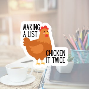 May include: A sticker featuring a cartoon chicken with the text "MAKING A LIST CHICKEN IT TWICE" in black. The chicken is brown with a red comb and yellow feet. The sticker is on a desk with a cup of coffee and pencils.