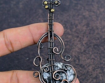 May include: A handcrafted pendant in the shape of a violin. The pendant features a black and white stone base, with copper-colored wire forming the body and decorative swirls. Small gold-colored beads accent the top.