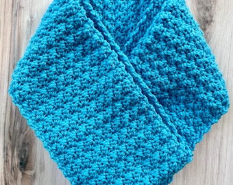 May include: A turquoise blue crocheted cowl scarf. The scarf is made with a textured stitch, creating a dense and warm fabric. The cowl is folded over, showcasing the intricate stitch pattern and the vibrant color.