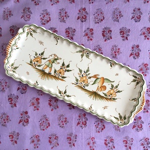 May include: A white rectangular serving platter with a scalloped edge. The platter is decorated with hand-painted green and yellow floral designs and two figures in the center.