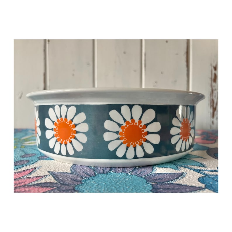 May include: A white ceramic bowl with a blue and white daisy pattern. The daisies have orange centers.