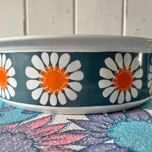 May include: A white ceramic bowl with a blue and white daisy pattern. The daisies have orange centers.