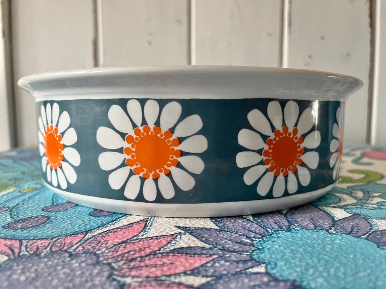 May include: A white ceramic bowl with a blue and white daisy pattern. The daisies have orange centers.