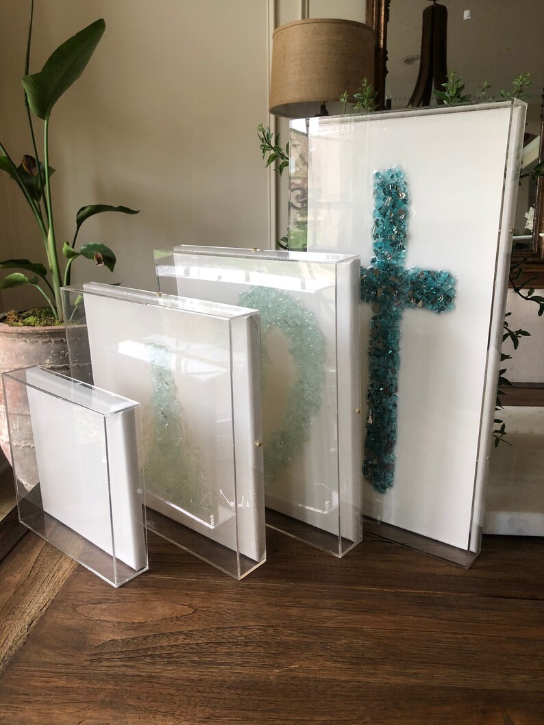 May include: Four clear acrylic frames with white mats and different sized canvases. The largest canvas features a turquoise blue cross made of glass mosaic tiles.