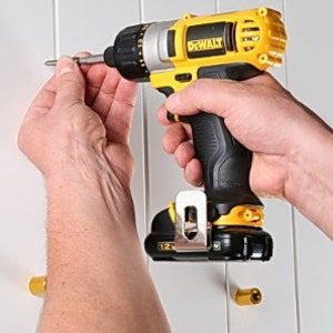 May include: A yellow and black cordless drill with a black and silver drill bit. The drill is being used to screw a screw into a white wall.