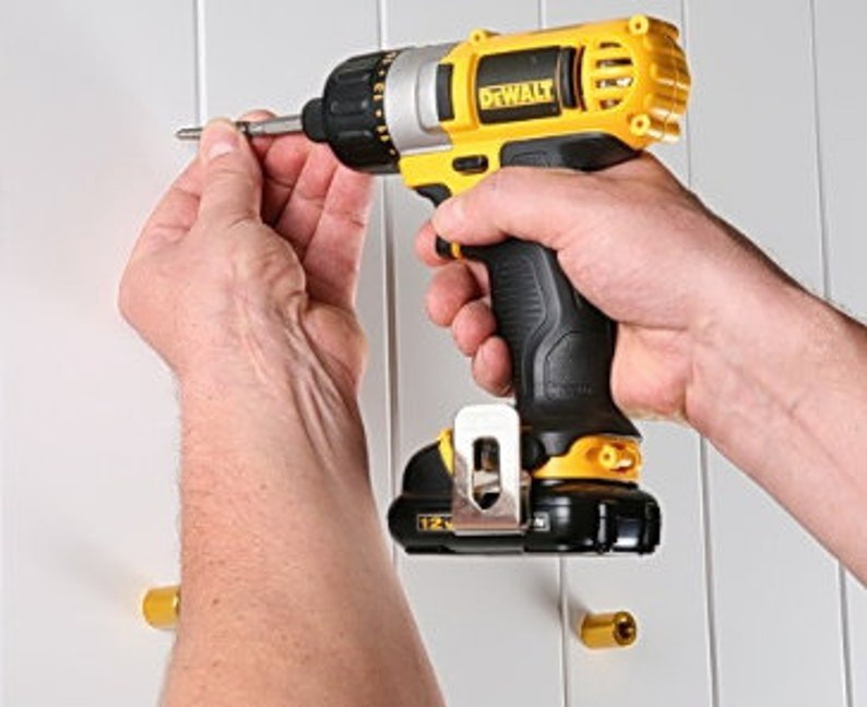 May include: A yellow and black cordless drill with a black and silver drill bit. The drill is being used to screw a screw into a white wall.