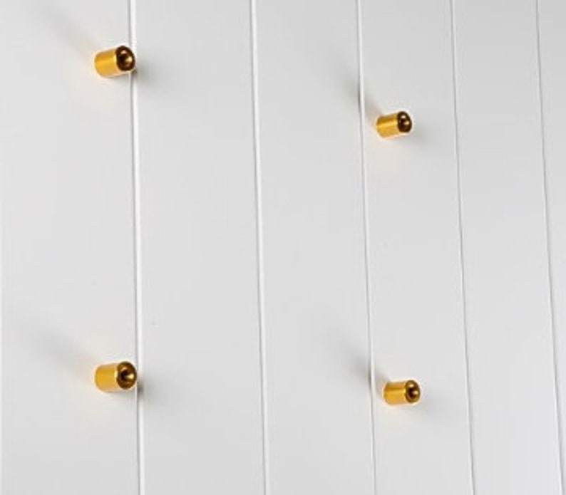 May include: Four gold-coloured metal knobs mounted on a white wall.