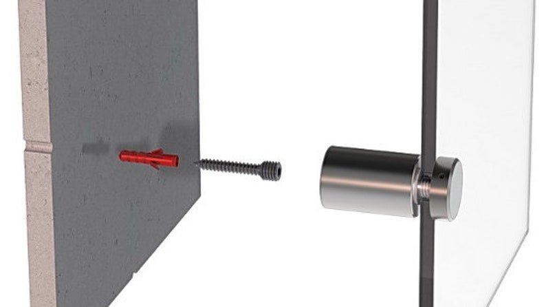 May include: A close-up of a glass panel being mounted to a wall using a metal bracket and a screw. The screw is attached to a red plastic anchor in the wall.