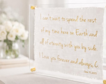 May include: A clear acrylic frame displays a white fabric with gold lettering. The text says, "I can't wait to spend the rest of my time here on Earth and all of eternity with you by side. I love you forever and always, C. June 11, 2023."