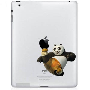 Puede incluir: iPad blanco con un logotipo de Apple negro y una pegatina de un panda blanco y negro que lleva un atuendo amarillo y naranja y patea un balón de fútbol.