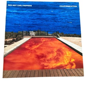 May include: Album cover for Red Hot Chili Peppers' Californication. The image features a pool of red water against a backdrop of blue ocean and sky. The album title and band name are printed at the top.